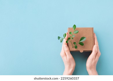 Woman hands holding cardbox from natural recyclable materials with green leaves sprout on blue table top view. Responsible consumption, eco friendly packaging, zero waste concept. - Shutterstock ID 2259260337