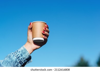 Woman hands holding a cup of coffee over blue sky background. Hipster girl holding paper cup with coffee take away. Paper coffee cup in woman hands with perfect manicure. - Shutterstock ID 2112616808