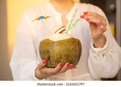  Woman Hands  Holding  Fresh  Green Coconut Drink With Paper Straw  And Rainbow Umbrella   On Tropical  Sunset Background . Vacation  Exotic  Travel Destinations  Concept .