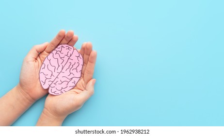 Woman hands holding human brain shape made from paper on light blue background. Awareness of Alzheimer, Parkinson's disease, dementia, stroke, seizure or mental health. Neurology and Psychology care.