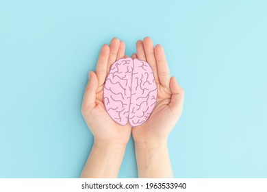 Woman hands holding human brain shape made from paper on light blue background. Awareness of Alzheimer, Parkinson's disease, dementia, stroke, seizure or mental health. Neurology and Psychology care.