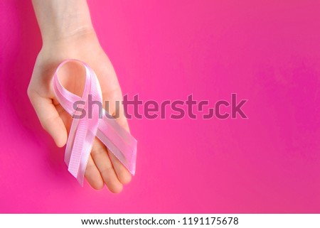 Woman hands holding pink colored ribbon - international symbol of breast cancer awareness and moral support for illness survivors. Isolated background, copy space, close up, top view fat lay.