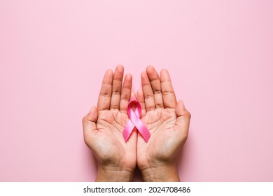 Woman hands holding pink ribbon over pink background, breast cancer awareness, October pink concept - Shutterstock ID 2024708486