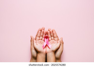 Woman hands holding pink ribbon over pink background, breast cancer awareness, October pink concept - Shutterstock ID 2025574280