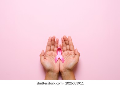 Woman hands holding pink ribbon over pink background, breast cancer awareness, October pink concept - Shutterstock ID 2026053911