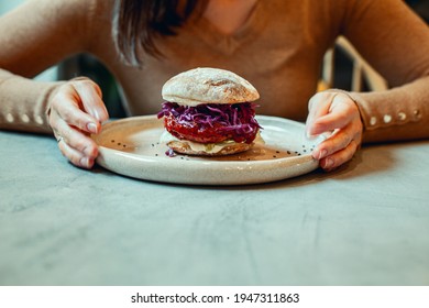 Woman Hands Holding Plate Of Vegetarian Burger With Beetroot, Lentil And Red Cabbage On Gluten Free Toasted Bun. Organic And Wellbeing Product Concept. Healthy Lifestyle And Dieting. Copy Space