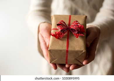 Woman hands holding present with red bow.