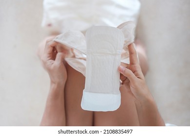 Woman Hands Holding Sanitary Pad Or Menstruation Napkin During Wearing It. Menses, Feminine, Menstrual Period, Monthly Period And Personal Hygiene Concepts