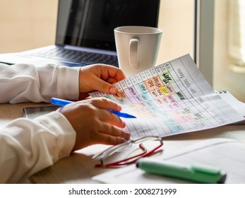 Woman hands holding a schedule with time blocking tasks for productivity and time management. Work desk with laptop, coffee cup, glasses and colorful weekly planning. Remote work from home