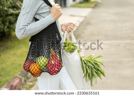 Woman hands holding shopping bag fruits and vegetables on the way home. Reusable cotton and mesh eco bags for shopping. Set zero waste plastic free concept. Sustainable lifestyle concept.