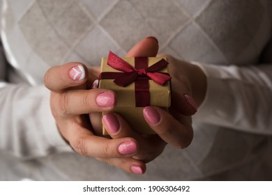 Woman Hands Holding A Small Present Box With Red Ribbon Over. Valentine Gift Box. Close Up Shot Of Female Hands.Shallow Depth Of Field With Focus On The Little Box.