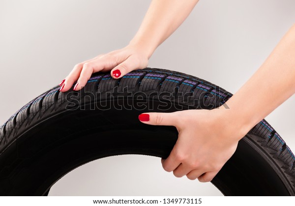 Woman hands holding snow tire\
isolated on grey background. Emancipation and femininity\
concept.