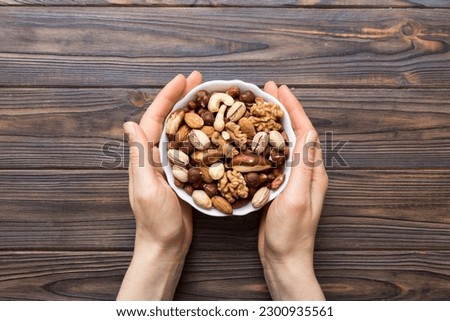 Woman hands holding a wooden bowl with mixed nuts Walnut, pistachios, almonds, hazelnuts and cashews. Healthy food and snack. Vegetarian snacks of different nuts.