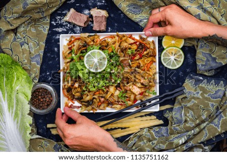 Woman hands holds with chopsticks asian fried noodles with vegetables, prawn and octopus meat cooked in soy sauce. Traditional authentic food in asian cafe or restaurant. Eat with chopsticks