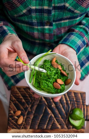 Woman hands holds fresh green Italian mediterranean pesto dip with basil, rocket salad, olive oil, lemon. Dips garlic sprout. Organic natural ingredients. Top view. Raw healthy vegan, vegetarian food 