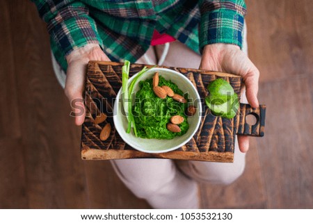 Woman hands holds fresh green Italian mediterranean pesto dip with basil, rocket salad, olive oil, lemon, garlic. Organic natural product ingredients. Top view. Raw healthy vegan, vegetarian food 