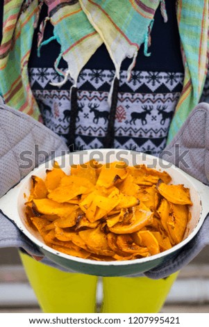 Woman hands holds homemade baked pumpkin chips with paprika made in oven on iron cast pan. Crispy, spicy with crunchy crust.