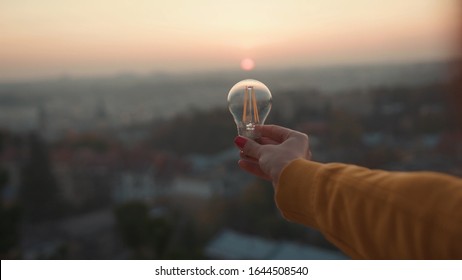 Woman hands holds a house light bulb at sunset renewable energy nature electricity innovation green invention responsibility environment adult power protect lamp slow motion