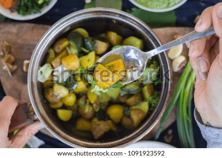 Woman hands holds and mix stewed, steamed, cooked veggies. New potatoes, eggplant, spinach leaves with garlic and herbs. Soy meat with salsa ketchup hot sauce. Raw vegan vegetarian healthy food