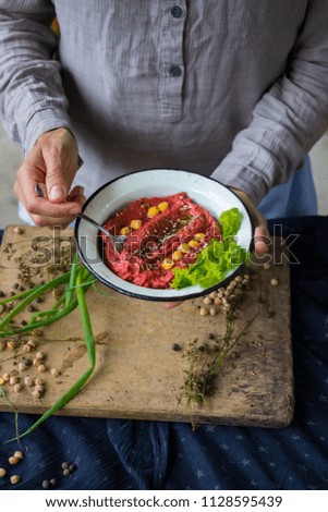 Woman hands holds spicy red beetroot Israeli chickpea hummus with herbs and covered with olive oil. Traditional mediterranean food used with vegetables. Vegan vegetarian healthy food.