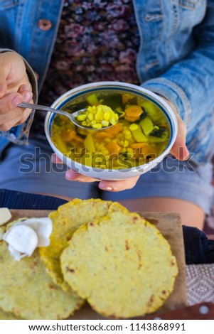 Woman hands holds vegetable corn soup with turmeric powder. Vegetarian lunch or vegan dinner with carrot and potato. Served with Indian traditional garlic naan flat bread or chapati (roti).