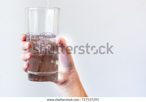 グレイと白の背景にガラスに水を注ぎながら 水をグラスに持つ女性の手 コップ1杯の水 の写真素材 今すぐ編集