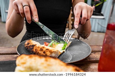 woman hands with knife and fork cutting pizza on table in cafe outdoor