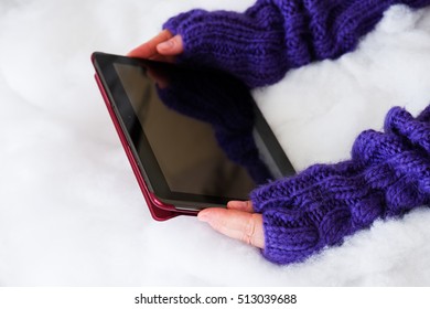 Woman Hands In Light Teal Knitted Mittens Are Holding Modern Tablet Pc On Snow Background. Winter Concept.