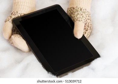 Woman Hands In Light Teal Knitted Mittens Are Holding Modern Tablet Pc On Snow Background. Winter Concept.