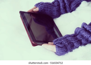 Woman Hands In Light Teal Knitted Mittens Are Holding Modern Tablet Pc On Snow Background. Winter Concept.