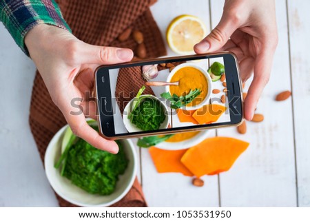 Woman hands makes phone food photo of lunch or dinner with creamy pumpkin soup dip squash on wooden board with vegetables. Photography for social networks post. Raw, vegan, vegetarian food