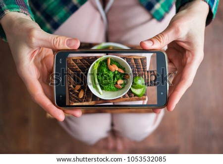 Woman hands makes phone food photo of lunch or dinner with Italian pesto dip with basil, rocket salad on wooden board with vegetables. Photography for social networks post. Raw, vegan, vegetarian food
