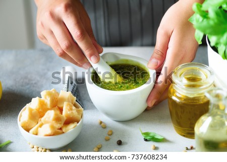 Woman hands making italian pesto in bowl. Ingredients - basil, lemon, parmesan, pine nuts, garlic, olive oil and salt on rustic wooden background. Top view, flat lay, copyspace