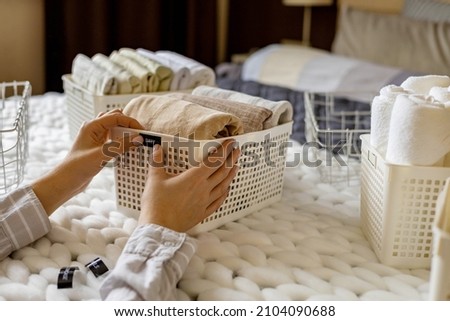 Woman hands neatly folded linens and towels use Marie Kondo method with sticky label tags top view closeup. Female housewife arms sticking names on case box for comfortable storage in bedroom closet
