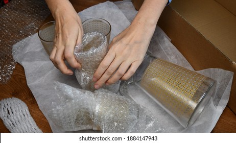 Woman hands pack up breakable fragile glassware and wrap into wrapping bubble plastic in preparation to move to new home. Packing up jug and drink glassses