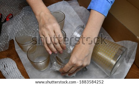 Woman hands pack up breakable fragile glassware into wrapping bubble plastic and put into cardboard box in preparation to move to new home. Packing up jug and drink glassses