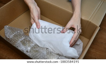 Woman hands pack up fragile tableware into wrapping bubble plastic and put into cardboard box in preparation to move to new home