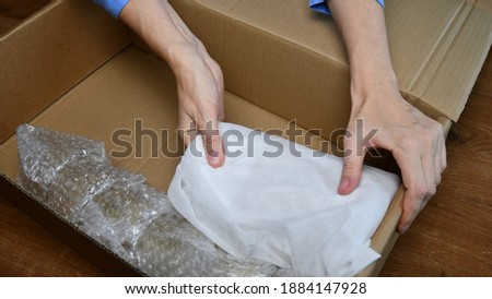 Woman hands pack up fragile tableware into cardboard box and fix wrapped household items inside. Preparation for moving day