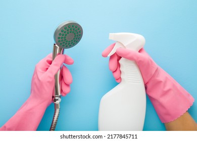 Woman hands in pink protective rubber gloves holding white plastic spray bottle and shower head on light blue table background. Pastel color. Limescale removing. Closeup. Point of view shot.