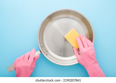 Woman hands in pink rubber protective gloves washing stainless frying pan with yellow sponge on light blue table background. Closeup. Pastel color. Point of view shot. - Powered by Shutterstock