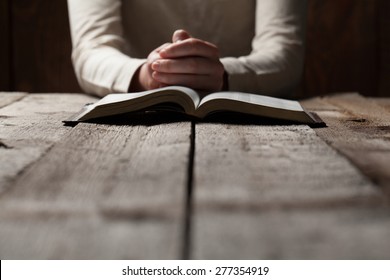 Woman hands praying with a bible in a dark over wooden table