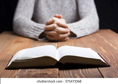 Woman hands praying with a bible in dark over wooden table