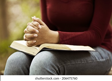 Woman hands praying with a bible in his legs Outdoors