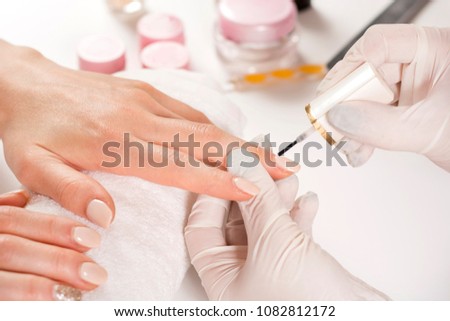 Woman hands with protect gloves painting finger nails in manicure studio. Close up, selective focus.