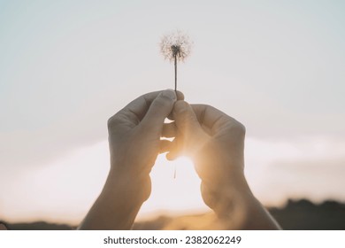 Woman hands raising up a dandelion flower against the sky. Nature and people lifestyle. Daydreaming and hope. Feeling and happiness. Soft and love. Romantic image with nature. Freedom environment - Powered by Shutterstock