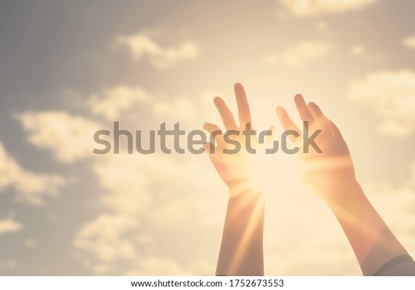 Woman hands reaches for the sky and\
closes the sun, the sun\'s rays pass through the\
hand