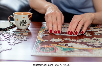 Woman hands with red nail polish putting jigsaw puzzle pieces together. Home quarantine. Coronavirus pandemic concept.