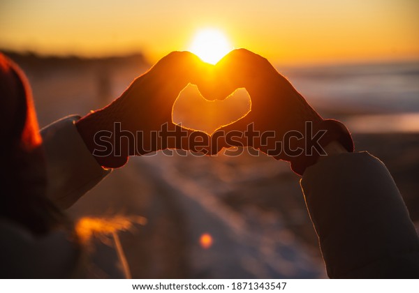 Woman hands in red winter gloves Heart symbol\
shaped Lifestyle, Winter Solstice and Feelings concept with sunset\
light nature on\
background
