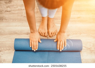 Woman hands rolled up yoga mat on gym floor in yoga fitness training room. Home workout woman close up hands rolling foam yoga gym mat. Woman barefoot home workout sportive healthy lifestyle concept - Powered by Shutterstock