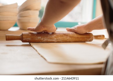Woman hands rolling out dough in flour with rolling pin in bakery.
